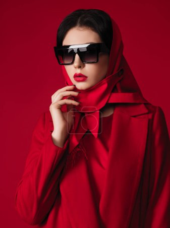 Foto de Modelo de moda roja total en abrigo y bufanda para la cabeza. Estudio de fotografía de ropa de marca. Mujer morena en traje casual. - Imagen libre de derechos