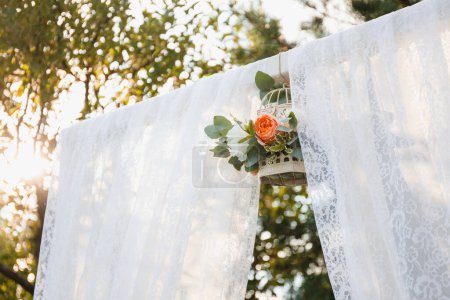Téléchargez les photos : Arche de mariage avec tulle et cage à oiseaux avec fleurs et lumière du soleil - en image libre de droit