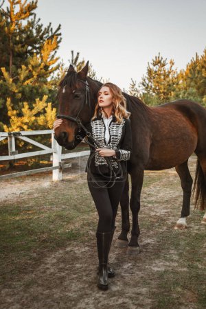 Photo for Beautiful woman model in black riding suit is standing on a farm with a horse - Royalty Free Image