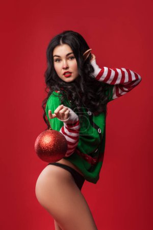 Téléchargez les photos : Jeune femme sexy en costume d'elfe et avec des oreilles elfiques dans le fond du studio rouge, style pin-up, vente du nouvel an - en image libre de droit