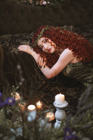 Foto de Fantasía mujer de pelo rojo con velas, flores y plantas, princesa druida fantasía oscura - Imagen libre de derechos