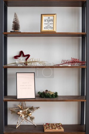 Photo for Bookcase with wooden shelves with Christmas decorations, photo frames with inscriptions, fir branches, star, box with Christmas toys, red and gold spangles - Royalty Free Image