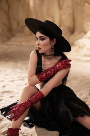 Foto de Hermosa mujer en ropa interior negra, sombrero y guantes de cuero rojo en el cañón, la marca de moda de tiro en las montañas - Imagen libre de derechos