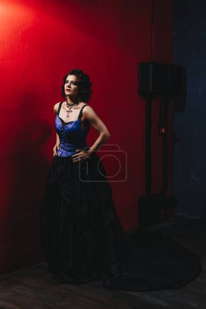 Foto de Hermosa mujer morena con maquillaje de noche violeta y peinado rizado, labios rojos, en un vestido de corsé negro y púrpura y con una gran cruz de diamantes, primer plano - Imagen libre de derechos