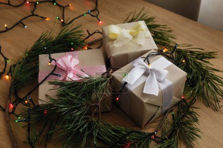 Foto de Regalo de Navidad en papel artesanal con cinta amarilla, ramas de pino, conos y una guirnalda en la mesa de madera - Imagen libre de derechos