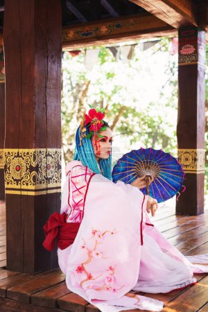 Téléchargez les photos : Belle femme avec dreadlocks bleu et costume japonais rose, assise sur le sol avec parapluie, festival asiatique, mode orientale - en image libre de droit