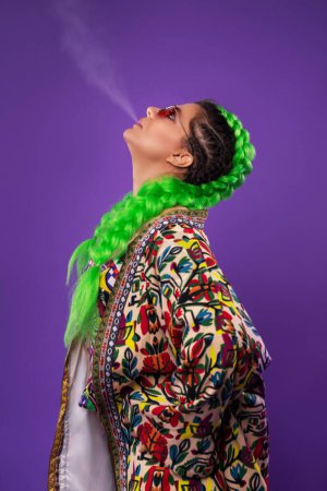 Photo for Studio portrait of smoking hippie woman with light green hair on purple background - Royalty Free Image