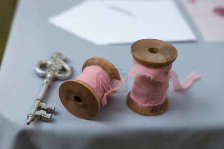Photo for Elegant retro wedding closeup of the rustic decoration, reels with pink ribbon, vintage key on the edge of the table with a blue tablecloth - Royalty Free Image