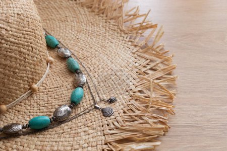 Photo for Women straw hat, vintage turquoise beads and a silver shell pendant lie on a wooden table, summer accessories - Royalty Free Image