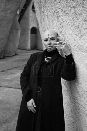 Foto de Retratos en blanco y negro de una chica calva con dibujos de runas en su cara de pie cerca de un hermoso edificio - Imagen libre de derechos