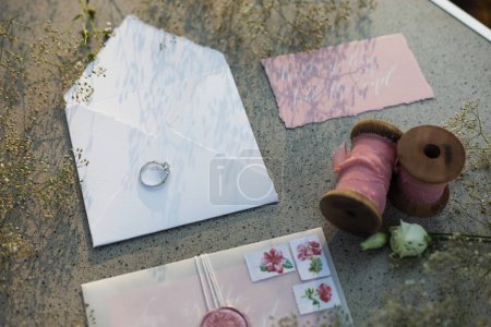 Photo for Outdoors vintage elegant rustic lovely wedding decor jewelry in summer spring, design, paper decor, white envelope with a bride's wedding ring on it, invitation cards, ribbon reel, flowers, sunset - Royalty Free Image