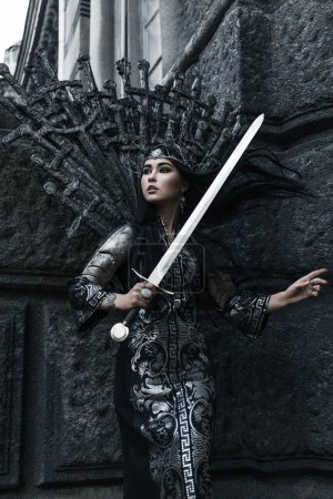 Téléchargez les photos : Belle femme brune dans une robe noire et argentée et armure avec décoration en forme d'épées, cheveux noirs, couronne, héros fantaisie, légende du nord - en image libre de droit