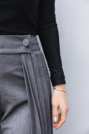 Foto de Detalle de ropa de mujer, falda-shorts grises, manos de mujer con pulseras y manicura, cuello alto negro, moda callejera - Imagen libre de derechos