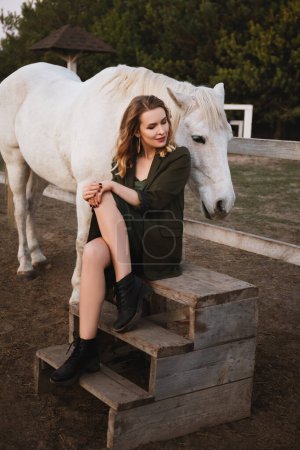 Téléchargez les photos : Belle femme assise près du corral avec des chevaux - en image libre de droit