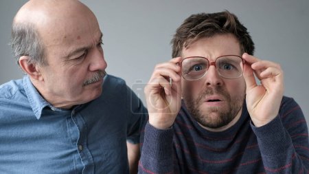 Sorprendidos hombres estupefactos maduro padre e hijo en grandes gafas con expresión WOW sobre fondo gris.