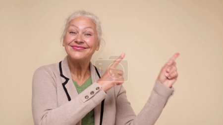 An caucasian elderly woman points her finger to attract attention on a beige background