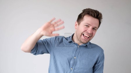 European young man waves his hand, greets his friends. Studio shot