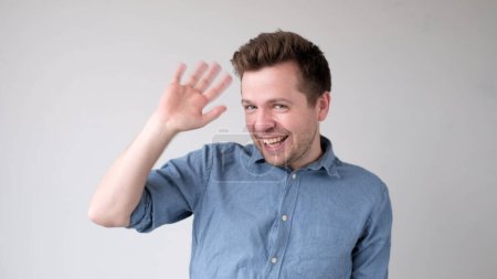 Europäischer junger Mann winkt mit der Hand, grüßt seine Freunde. Studioaufnahme