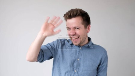 Europäischer junger Mann winkt mit der Hand, grüßt seine Freunde. Studioaufnahme