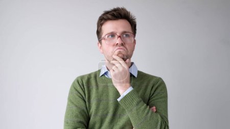 Foto de Un joven europeo se está frotando la barbilla en la duda, pensando y haciendo planes. Captura de estudio - Imagen libre de derechos