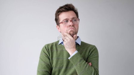 Foto de Un joven europeo se está frotando la barbilla en la duda, pensando y haciendo planes. Captura de estudio - Imagen libre de derechos