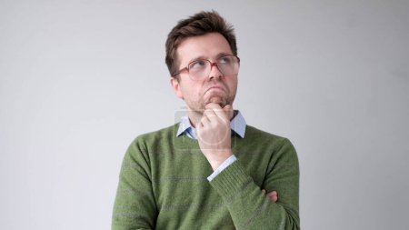 Photo for A European young man is rubbing his chin in doubt, thinking and making plans. Studio shot - Royalty Free Image