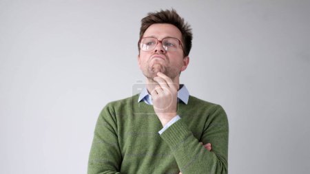 Photo for A European young man is rubbing his chin in doubt, thinking and making plans. Studio shot - Royalty Free Image