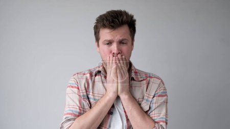 The tired European young man, lacking energy, closes his face with hands. He has no positive emotions. Studio shot