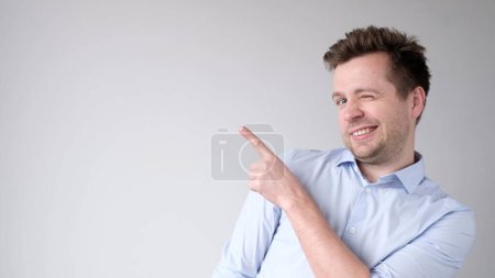 Photo for European young man points with his index finger towards an empty space for your advertisement - Royalty Free Image