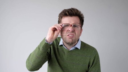 European young man with poor vision peers through his glasses, trying to discern the information that interests him. Studio shot