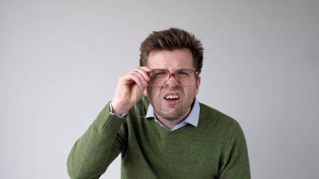 Europäischer junger Mann mit schlechter Sicht blickt durch seine Brille und versucht, die Informationen zu erkennen, die ihn interessieren. Studioaufnahme