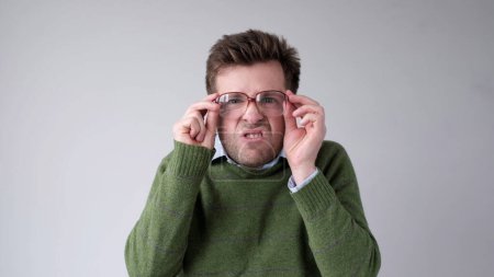 Un jeune Européen avec une mauvaise vision regarde à travers ses lunettes, essayant de discerner l'information qui l'intéresse. Plan studio