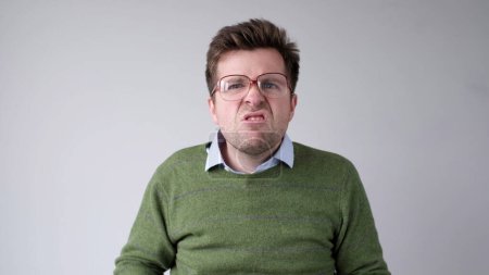 Europäischer junger Mann mit schlechter Sicht blickt durch seine Brille und versucht, die Informationen zu erkennen, die ihn interessieren. Studioaufnahme