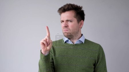Photo for European young man shakes his head in disagreement and says no, pointing his finger upwards. Studio shot - Royalty Free Image