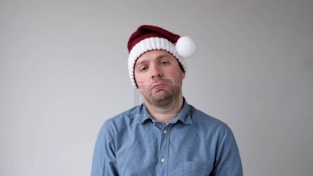 El triste y triste joven europeo en un sombrero de Año Nuevo mira sombríamente a la cámara. Decepciones en la celebración del Año Nuevo. Captura de estudio