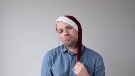 Photo for The sad and sorrowful European young man in a New Years hat looks gloomily into the camera. Disappointments in the New Year celebration. Studio shot - Royalty Free Image