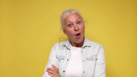 An elderly European woman is inspired, screaming wow and raising her hands in the air. Studio shot