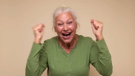An elderly European woman is inspired, screaming wow and raising her hands in the air. Studio shot