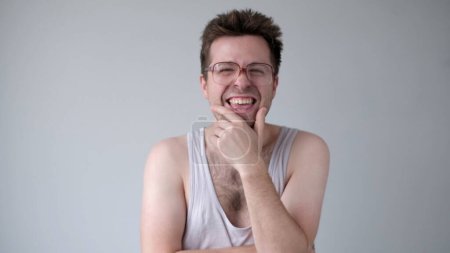 Un Européen sarcastique en grosses lunettes rit et pointe du doigt la caméra