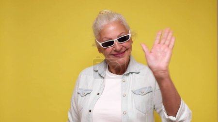 an elderly European woman greeting a friend, waving her hand and saying hello. Studio shot