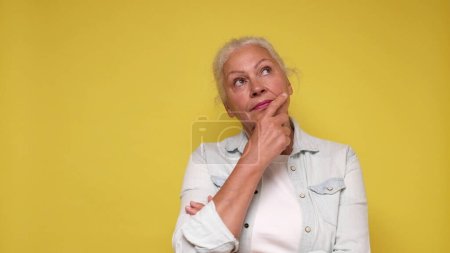 Elderly European woman is lost in thought, dreaming, and scratching her chin with her finger.
