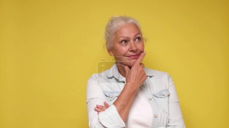 Elderly European woman is lost in thought, dreaming, and scratching her chin with her finger.