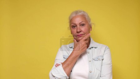 Photo for Elderly European woman is lost in thought, dreaming, and scratching her chin with her finger. - Royalty Free Image