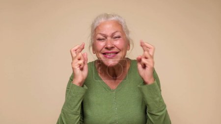 An elderly European woman crosses her fingers for good luck. Studio shot
