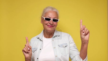 Une femme âgée caucasienne pointe du doigt pour attirer l'attention sur un fond beige