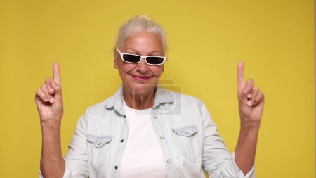 Eine kaukasische ältere Frau zeigt mit dem Finger auf beigen Hintergrund, um Aufmerksamkeit zu erregen