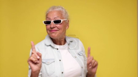 Elderly European woman in sunglasses is dancing. Studio shot