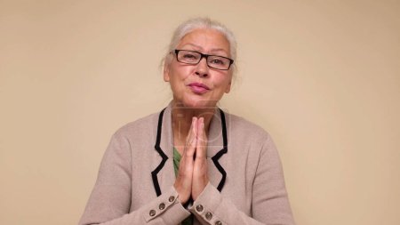 An elderly European woman is praying for help, holding her palms together. Do me a favor. Studio shot