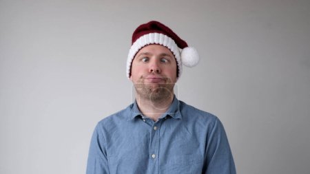 El triste y triste joven europeo en un sombrero de Año Nuevo mira sombríamente a la cámara. Decepciones en la celebración del Año Nuevo. Captura de estudio
