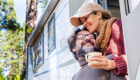 Romantic feeling moment with man and woman in tenderness outside a camper van with forest trees in background. Concept of happy and free lifestyle vacation for people. Man and woman in love outdoor